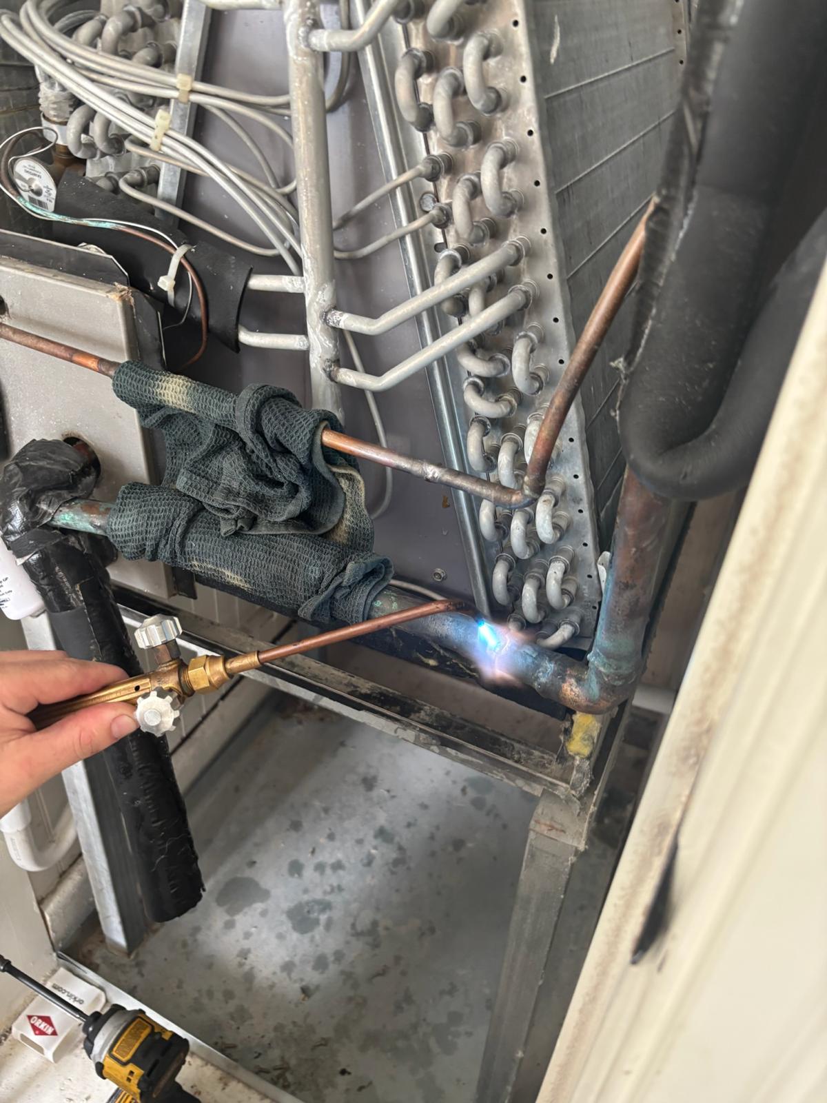 Air Force HVAC technician brazing copper refrigerant lines on an evaporator coil